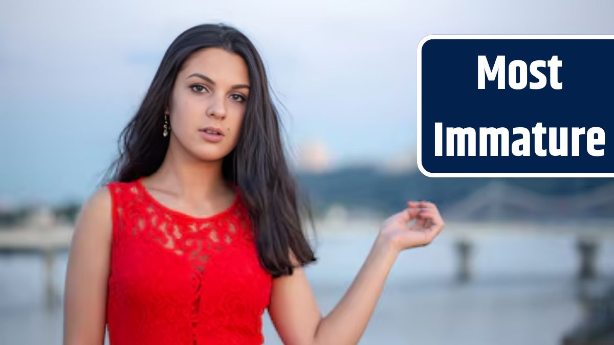 Beautiful young girl in a red dress posing on a bridge near an old fence. In the background there is a river, bridges and fragments of city buildings in the defocus.