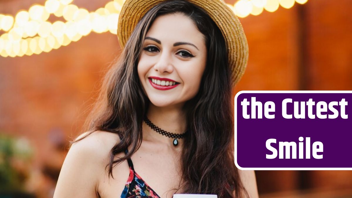 Young lady with makeup wearing straw hat necklace and dress holding paper cup with coffee smiling pleasantly at camera while posing at restaurant Woman with pleased expression resting at cafe